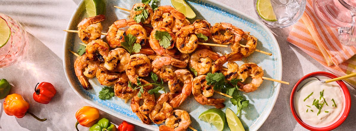 pale white and blue platter of Spicy BBQ Shrimp Skewers with Coconut Lime Yogurt on the side