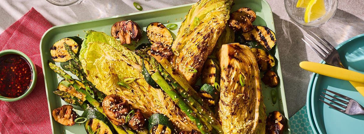 rectangular green vegetarian bbq platter of with grilled cabbage, mushrooms, zucchini and asparagus and a side bowl of spicy chili crisp