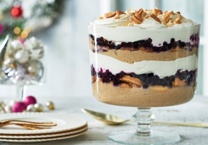 A glass trifle bowl filled with layers of pudding, cookies, cream, and fruit.