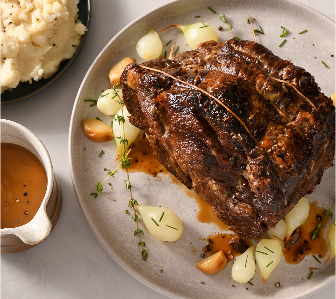 Pork shoulder blade roast on white plate with pearl onions