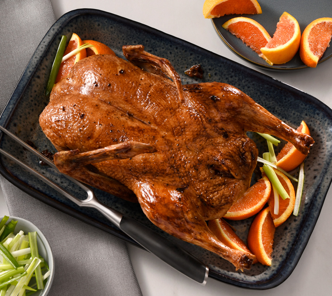 Roasted whole duck on black platter with side of oranges and green onion