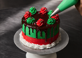 Green and Red Iced Cake with dripping chocolate ganache and red and green rosettes being added to the cake